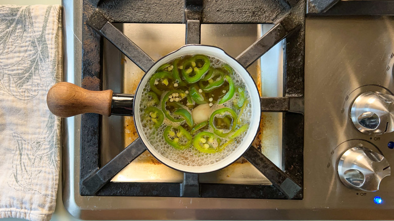 Sliced jalepenos cooking in brine in sauce pan on stovetop