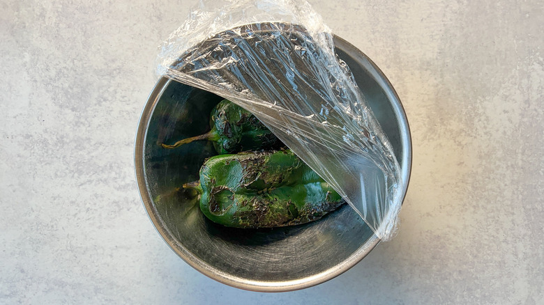 Steaming roasted poblano peppers in bowl with plastic wrap