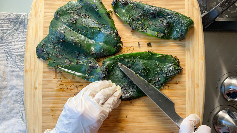 Scraping charred skins off roasted poblano peppers using knife and wearing gloves
