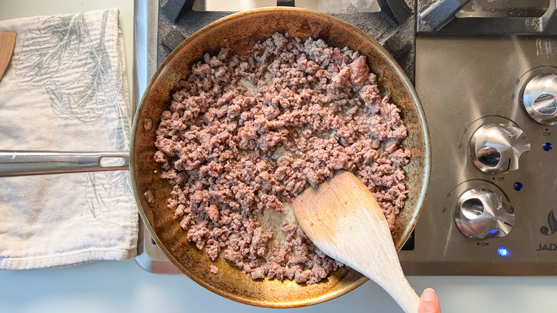Browning ground beef in skillet with wooden spoon