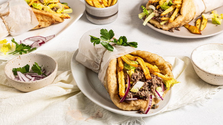Three ground beef gyros served on plates with side of fries and tzatziki