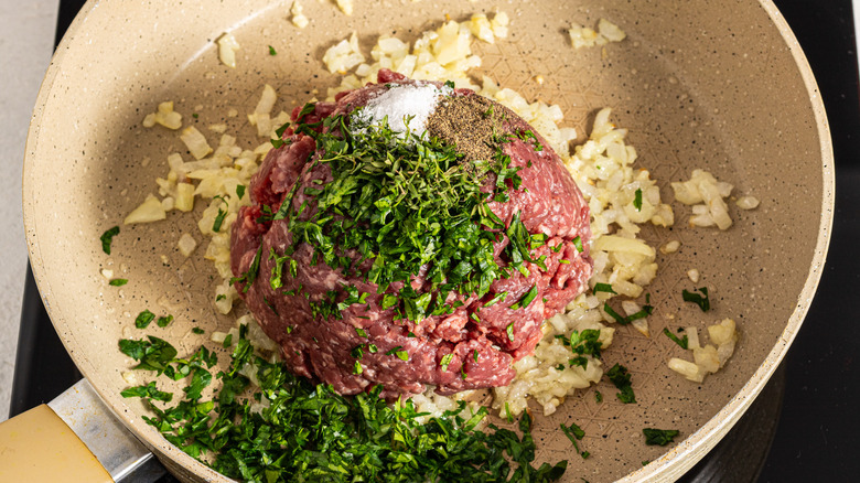 Skillet with ground beef, herbs, chopped onion, salt, and black pepper