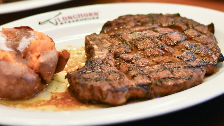 A steak with a sweet potato on a white plate
