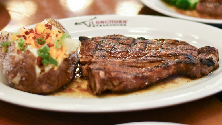 A steak with a loaded baked potato on a white plate