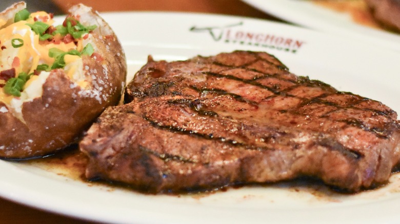 A steak next to a loaded baked potato on a white plate