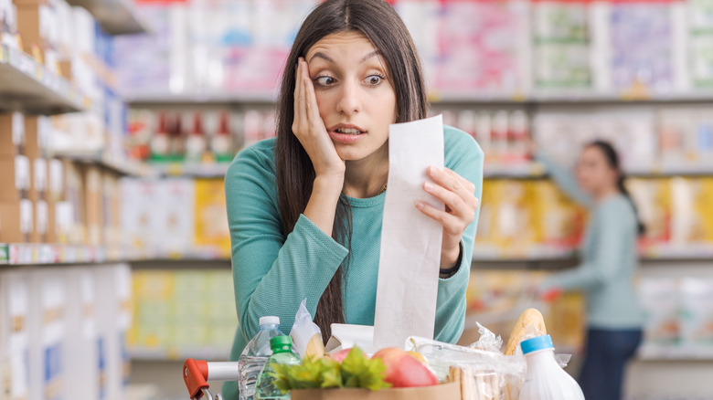 Shocked woman reads receipt at grocery store