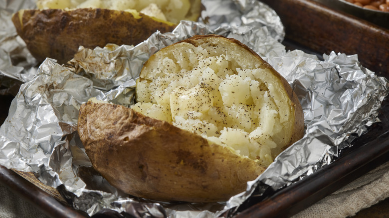 Peppered baked potatoes in foil on a baking sheet.