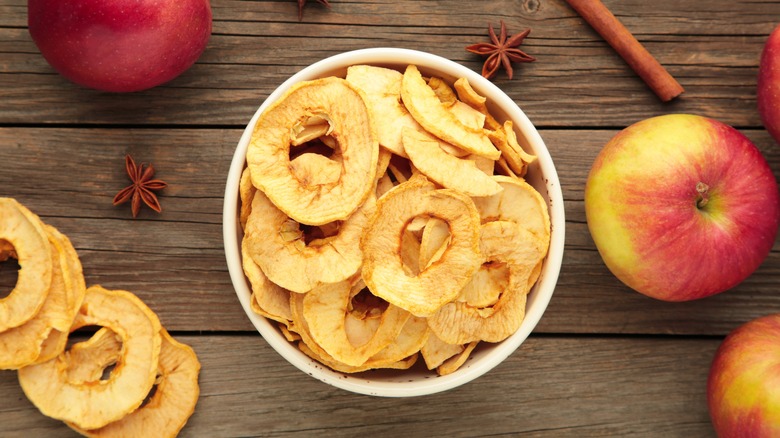 Bowl of apple chips surrounded by fresh apples and spices