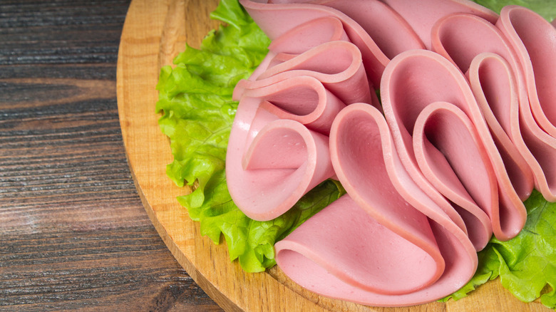 Sliced bologna with lettuce on a wooden board