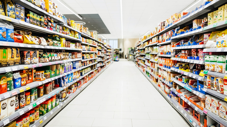 A brightly lit, fully stocked, long grocery store aisle