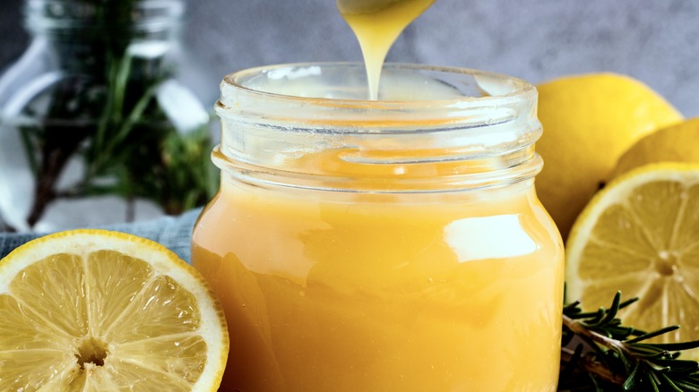 glass jar of lemon curd surrounded by lemons