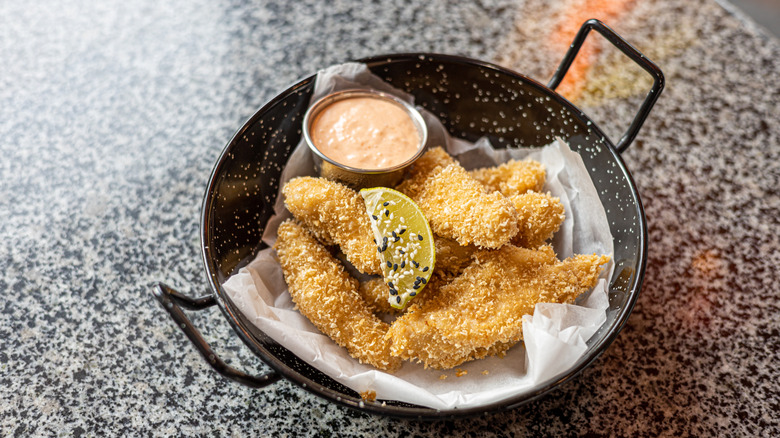 A serving of panko chicken pieces rests in a black dish.