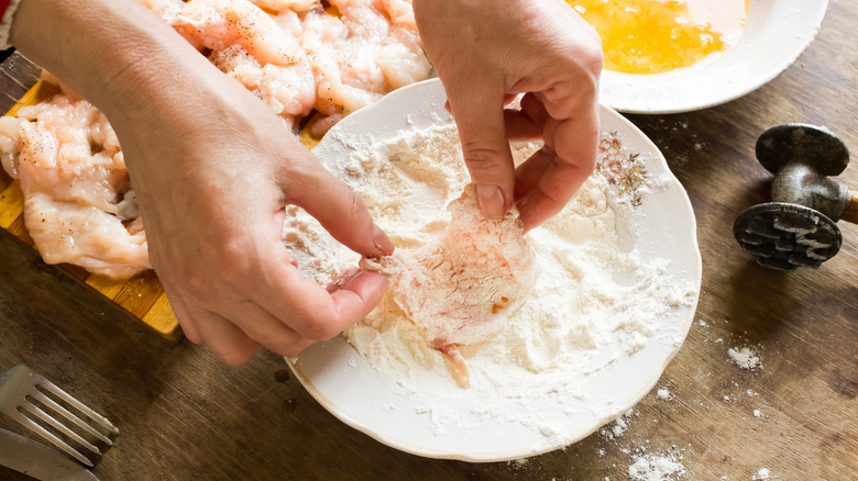 Person coating chicken in flour