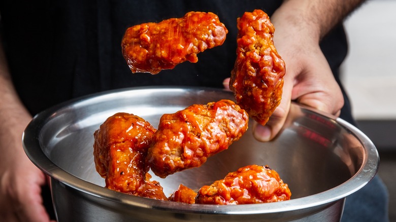 Person tossing chicken in sauce in a stainless steel bowl