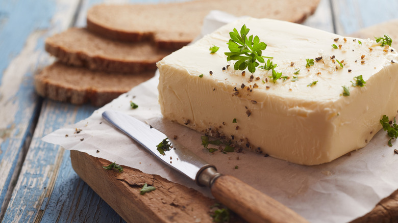 homemade butter with herbs on wooden tray next to butter knife