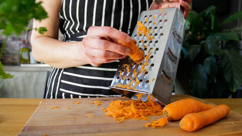 A person in an apron grating carrots with a hand grater.