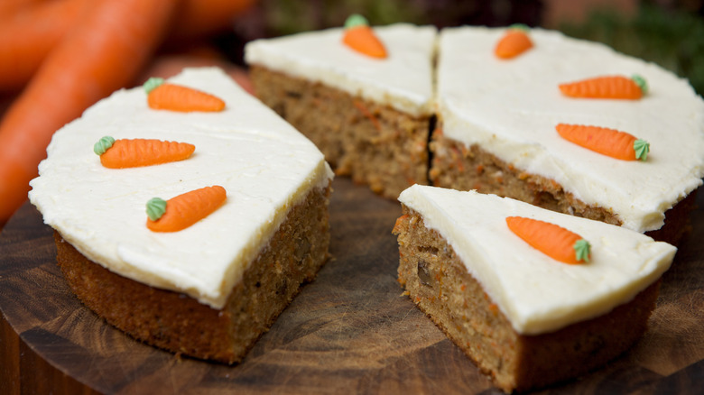 A round carrot cake cut into slices on a wooden cutting board.