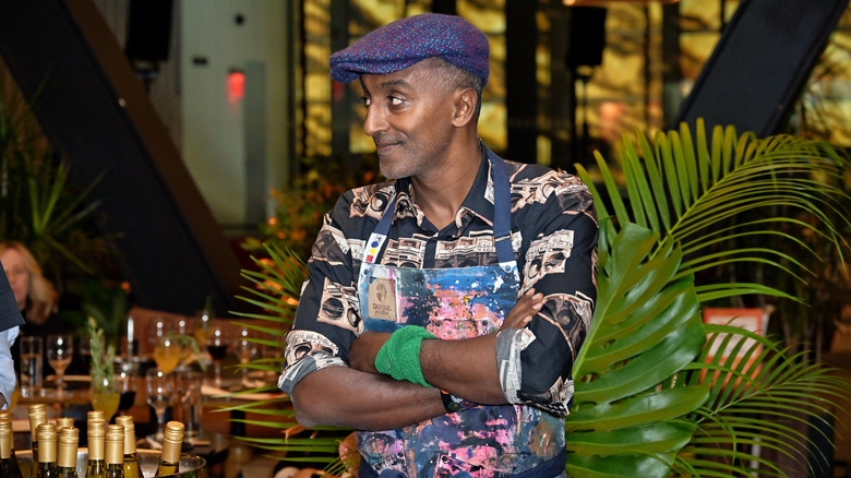 Marcus Samuelsson stands in a patterned apron with his arms crossed