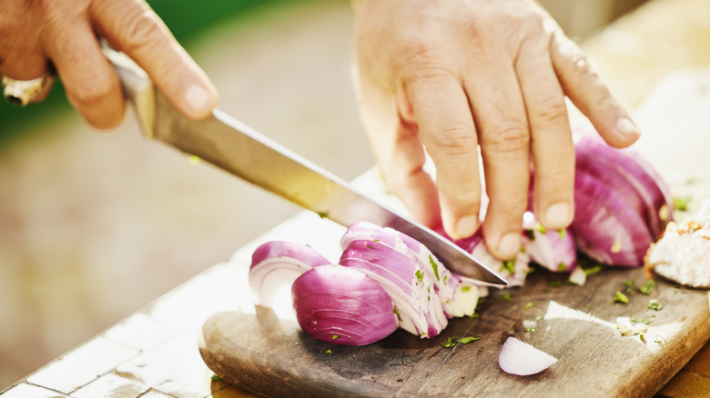 hands slicing red onion