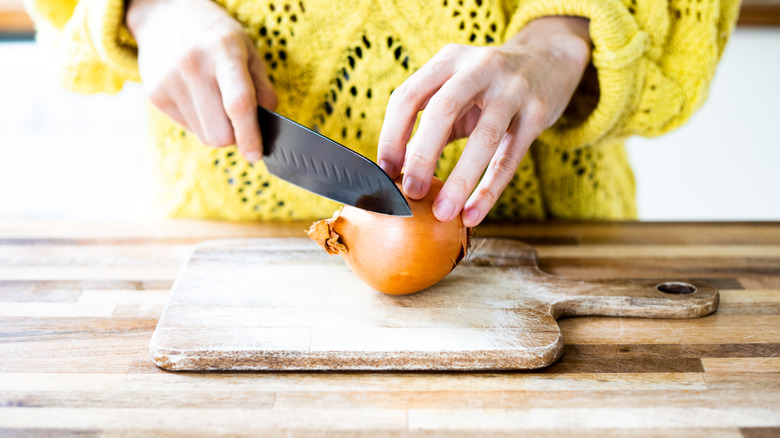 hand with onion on cutting board