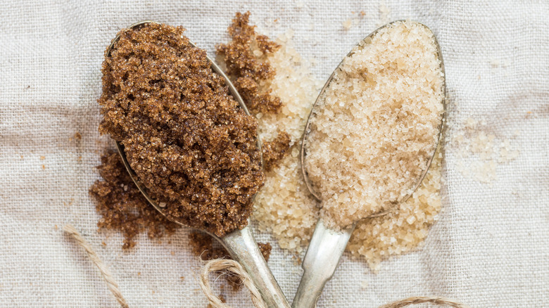 A spoonful of dark demerara sugar next to a spoonful of light muscovado sugar on light brown muslin.