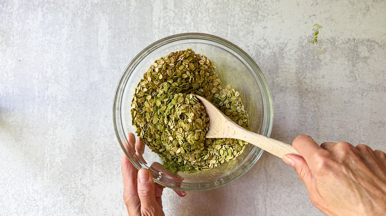 Mixing rolled oats, chia seeds, matcha powder and salt in large bowl with wooden spoon