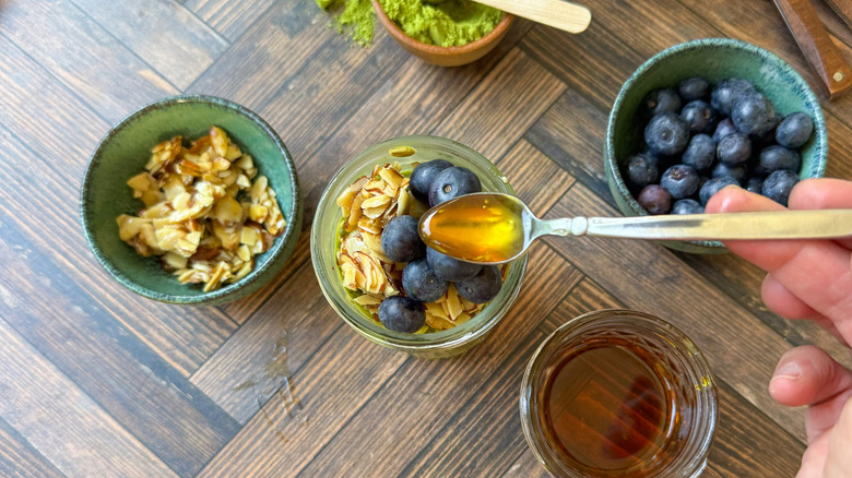 Drizzling maple syrup on match almond overnight oats with maple almonds and blueberries