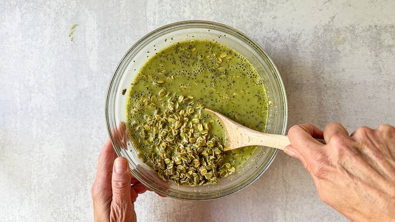 Mixing matcha almond overnight oats in glass bowl with wooden spoon