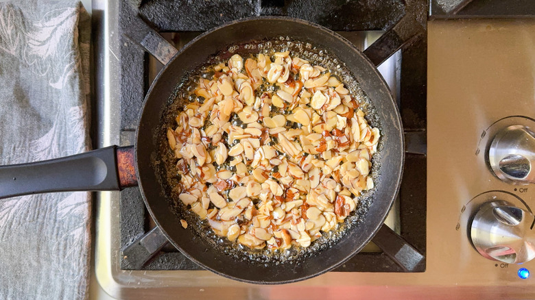 Sliced almonds cooking in maple syrup in skilled on stovetop