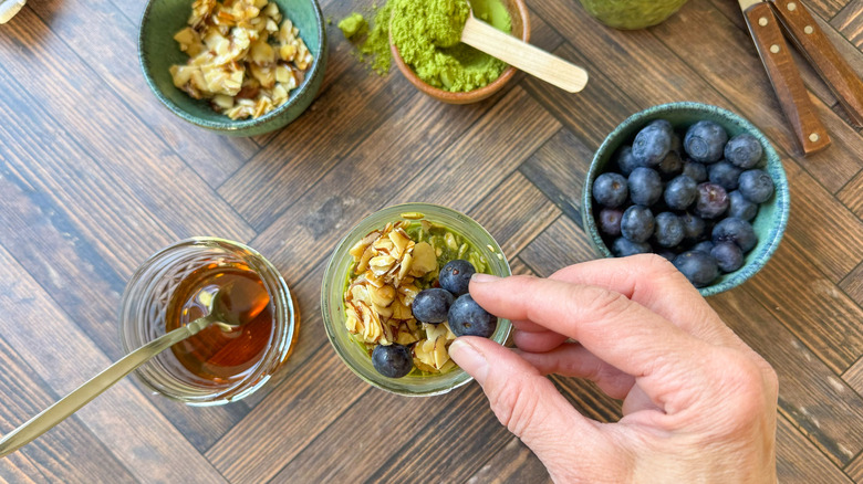 Adding maple almonds and fresh blueberries to matcha almond overnight oats in jar