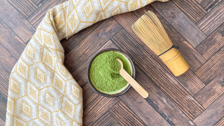 Matcha green tea powder in bowl with wooden spoon and whisk