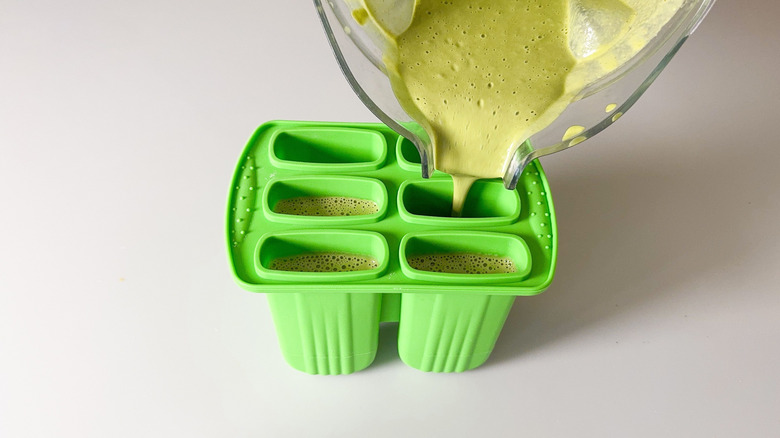 Pouring matcha pistachio popsicle mixture into popsicle molds