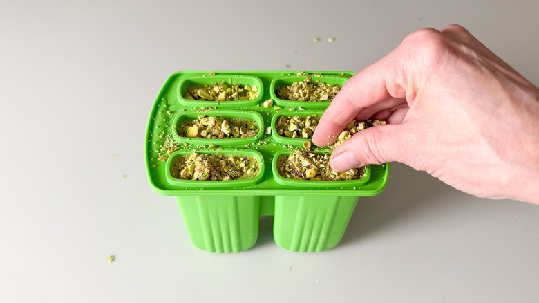 Sprinkling chopped pistachios on top of matcha pistachio popsicle mix in molds