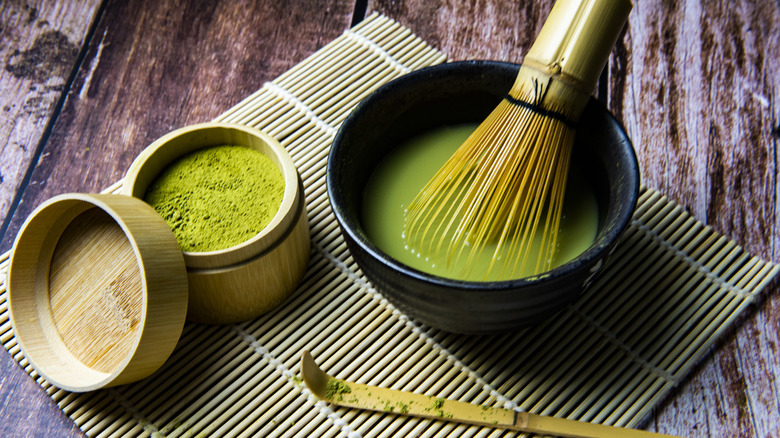 Whisk in bowl filled with matcha tea next to matcha powder