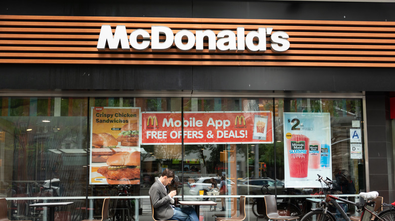Man sitting outside a McDonald's with window signs advertising mobile app and deals.
