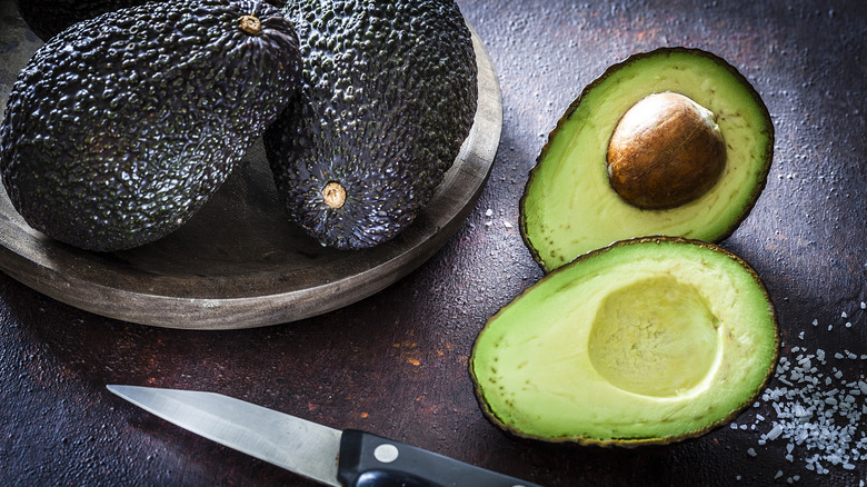 Cut avocado next to whole avocados, salt, and a knife