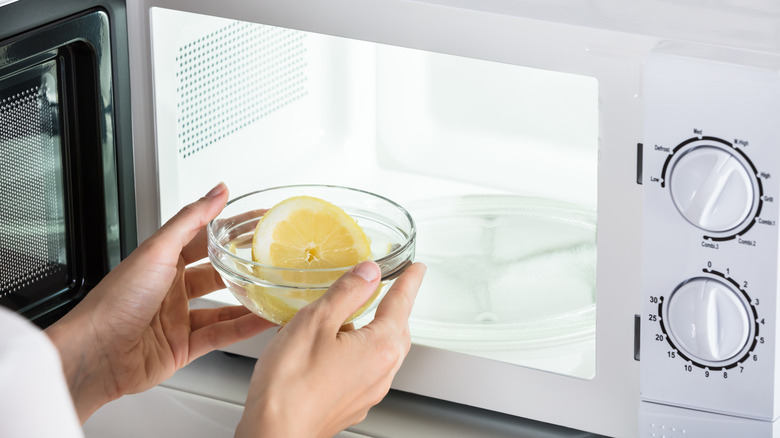 Hands placing a bowl with a half-cut lemon in to a microwave