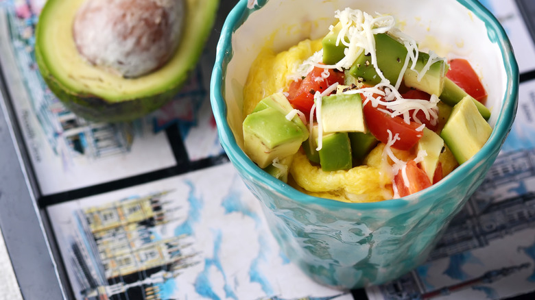 Mug with scrambled eggs topped with cheese, tomatoes, and avocado