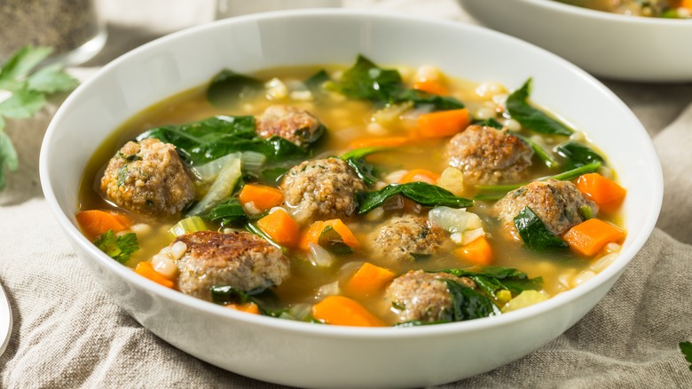 A bowl of Italian wedding soup with meatballs and leafy greens