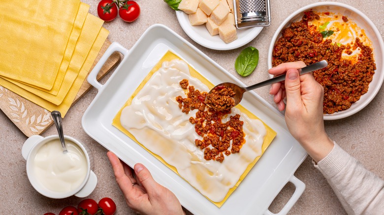 Person preparing lasagna with several ingredients