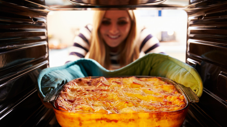 Smiling person taking lasagna out of oven 