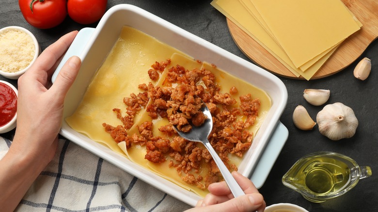 Person layering lasagna with meat sauce