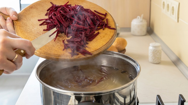 Person adding sliced beetroot to soup