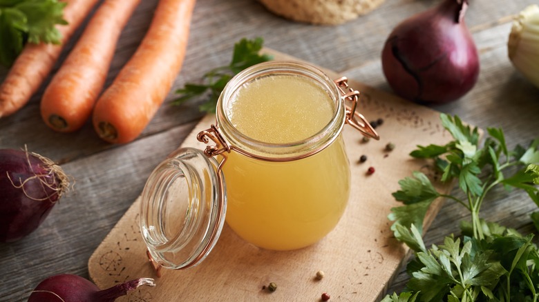 Jar of stock with vegetables on wooden board