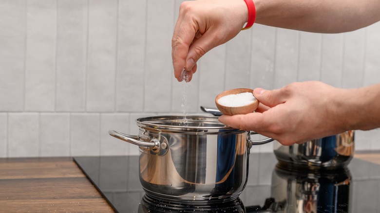 Person adding salt to metal pot