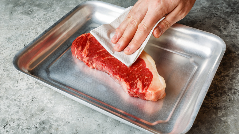 Patting steak dry with paper towels