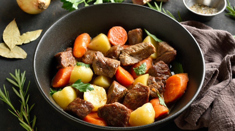 A black bowl of beef stew with potatoes and carrots, garnished with fresh herbs