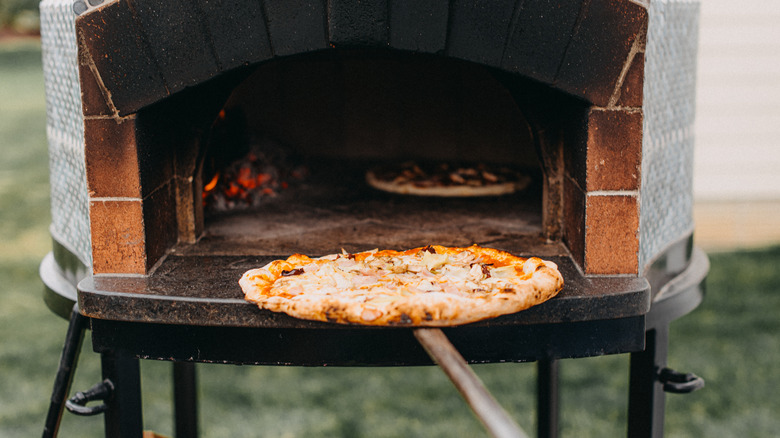 Chef puts a pizza in an outdoor oven