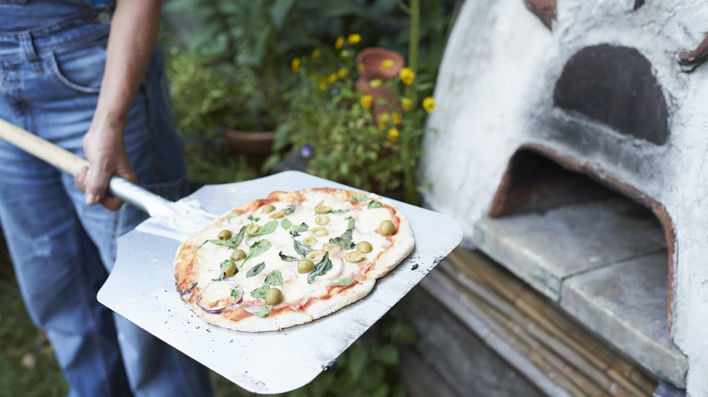 Olive pizza going in a pizza oven