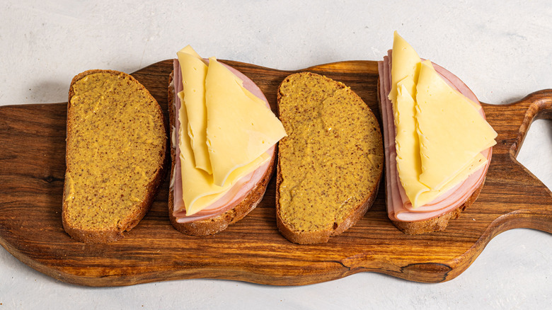 Four slices of bread, two with mustard and two with ham and cheese